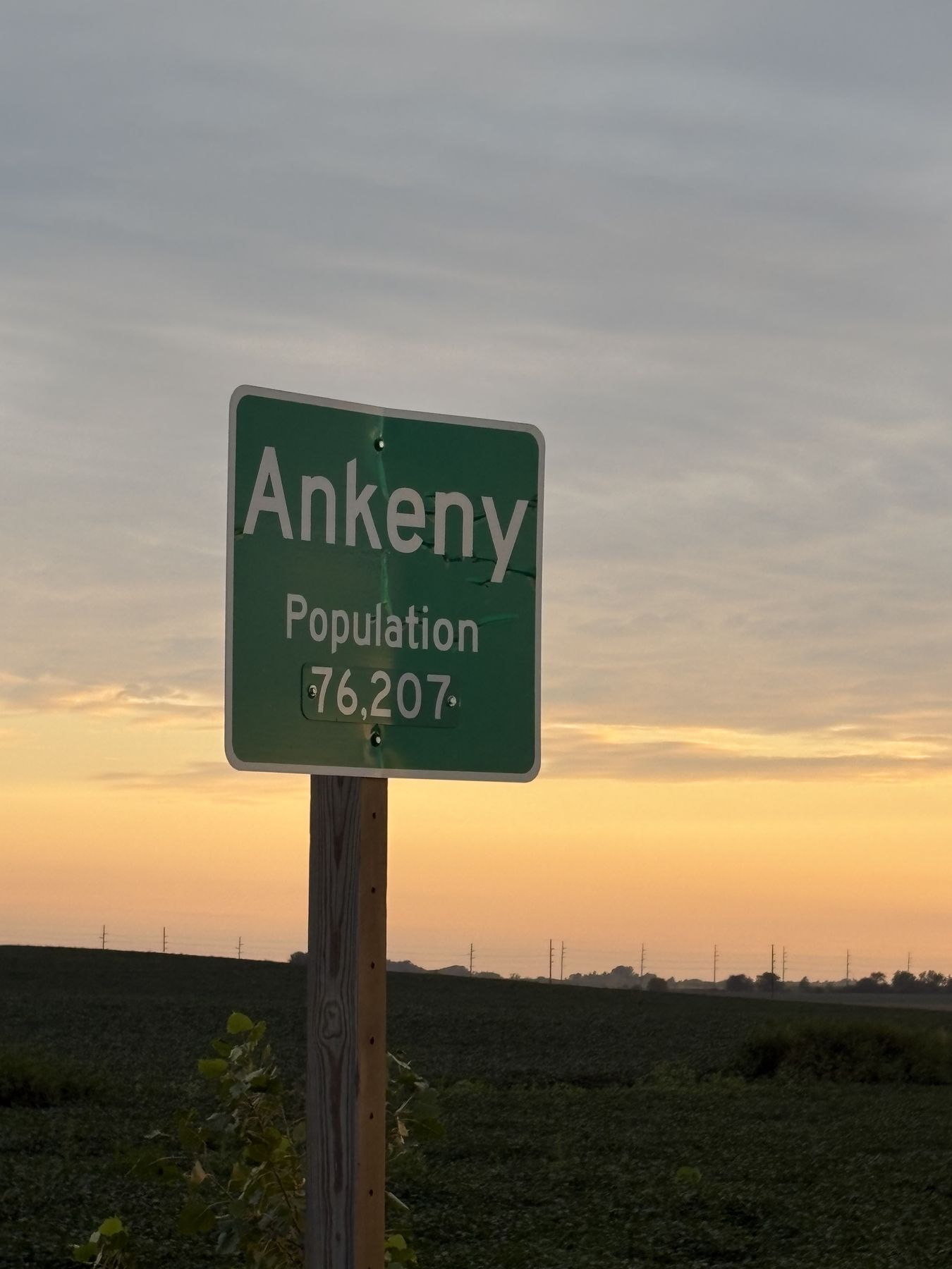 The Ankeny city-limits sign at golden hour, Population 76,207, on the edge of the soybean fields